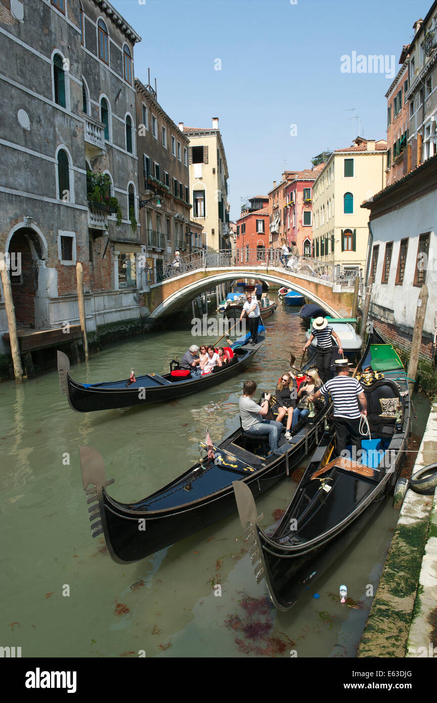 Venedig, Italien - APRIL 2013: Touristen Gondelfahrten passieren andere Gondeln mit Gondolieri auf einen kleinen Kanal. Stockfoto