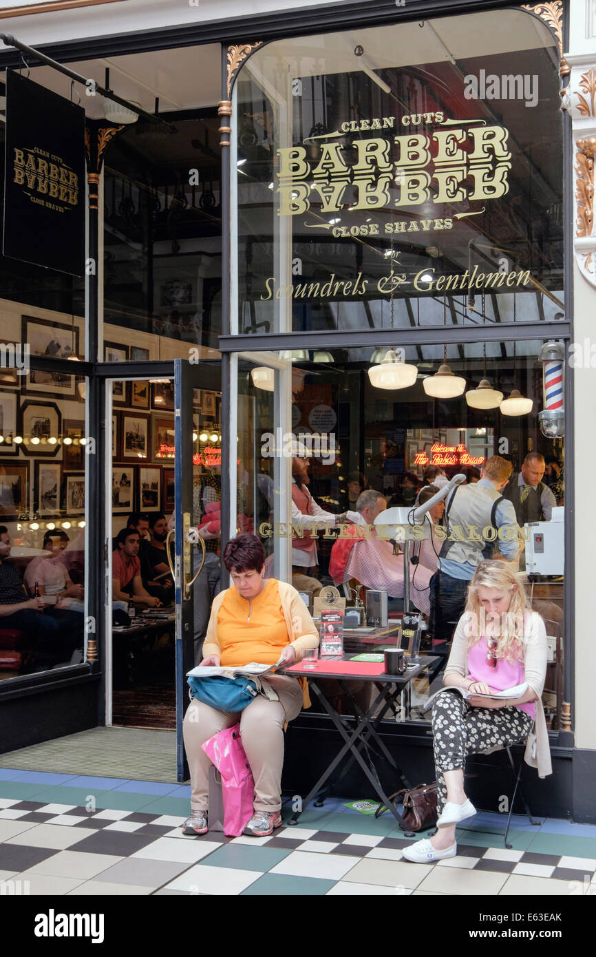 Zwei Frauen sitzen warten auf Männer außerhalb BarberBarber Herren nur Barbershop in Barton Arcade Manchester England UK Großbritannien Stockfoto