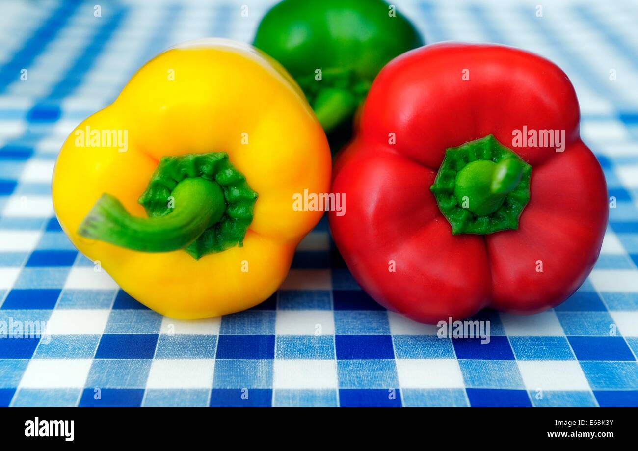 Eine rote gelbe und grüne Paprika auf blau kariertem Tischtuch Hintergrund Stockfoto