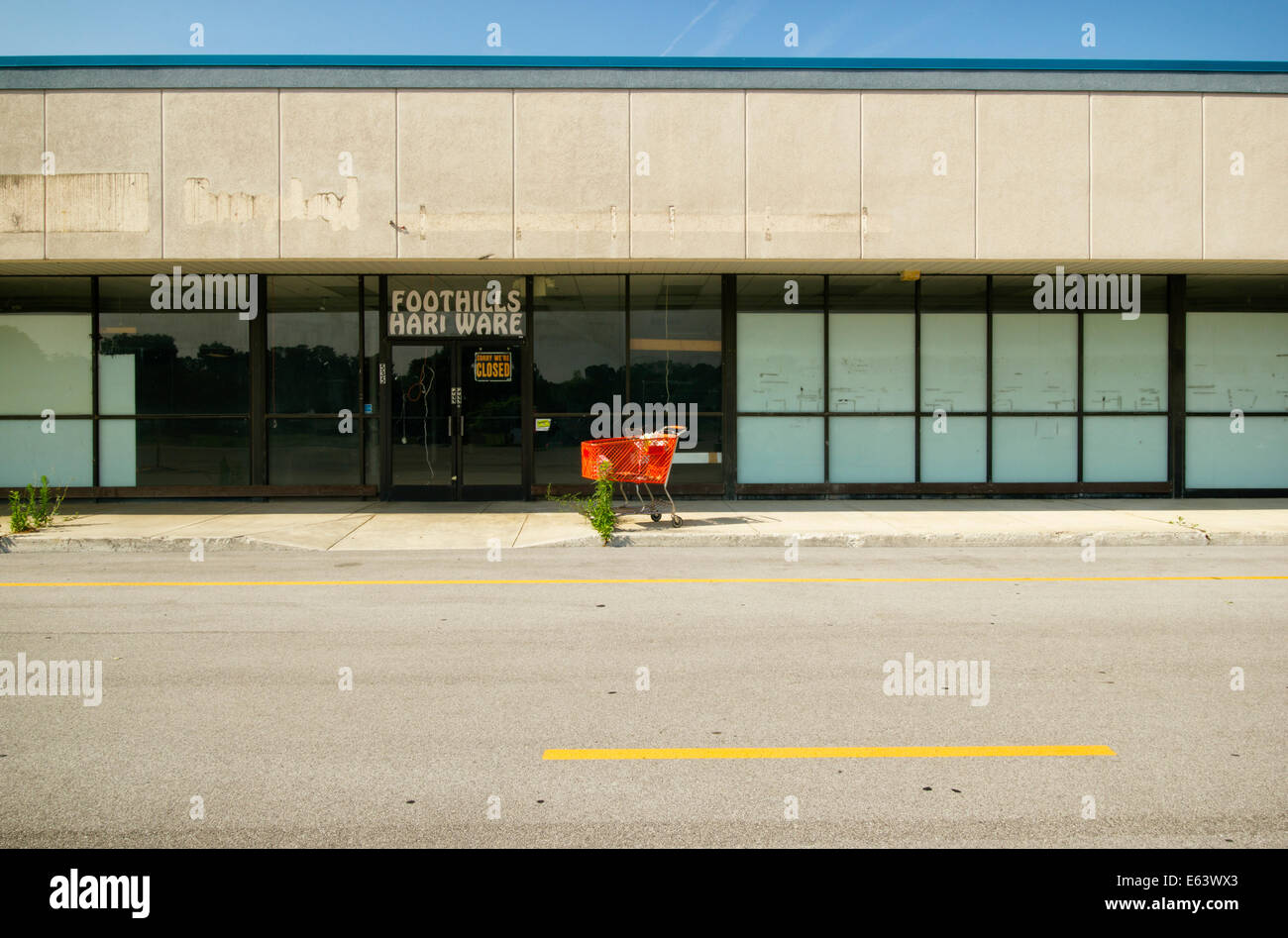 Eine leere Schaufenster in einem verlassenen Einkaufszentrum mit einem roten Einkaufswagen vor der Tür. Stockfoto