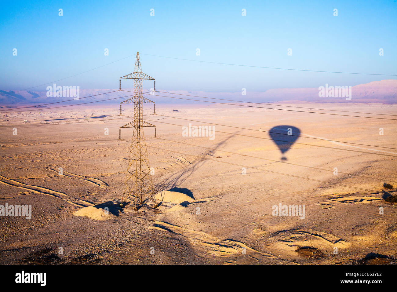 Der Schatten von einem Heißluftballon und einem Strommast über der Wüste von der West Bank des Nils in Ägypten bei Sonnenaufgang. Stockfoto