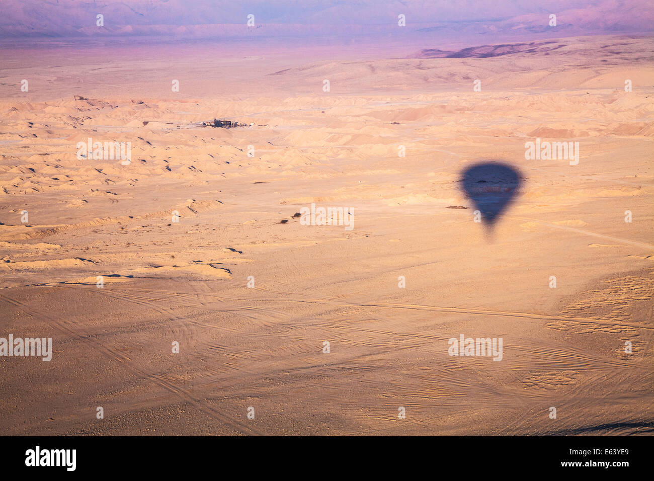 Der Schatten von einem Heißluftballon fliegen über der Wüste in Ägypten bei Sonnenaufgang mit einem kleinen Weiler in der Ferne. Stockfoto