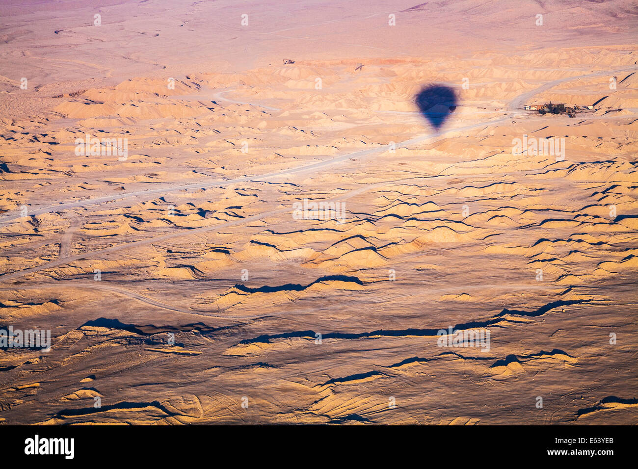 Der Schatten von einem Heißluftballon fliegen über der Wüste in Ägypten mit einem kleinen Weiler in der Ferne. Stockfoto