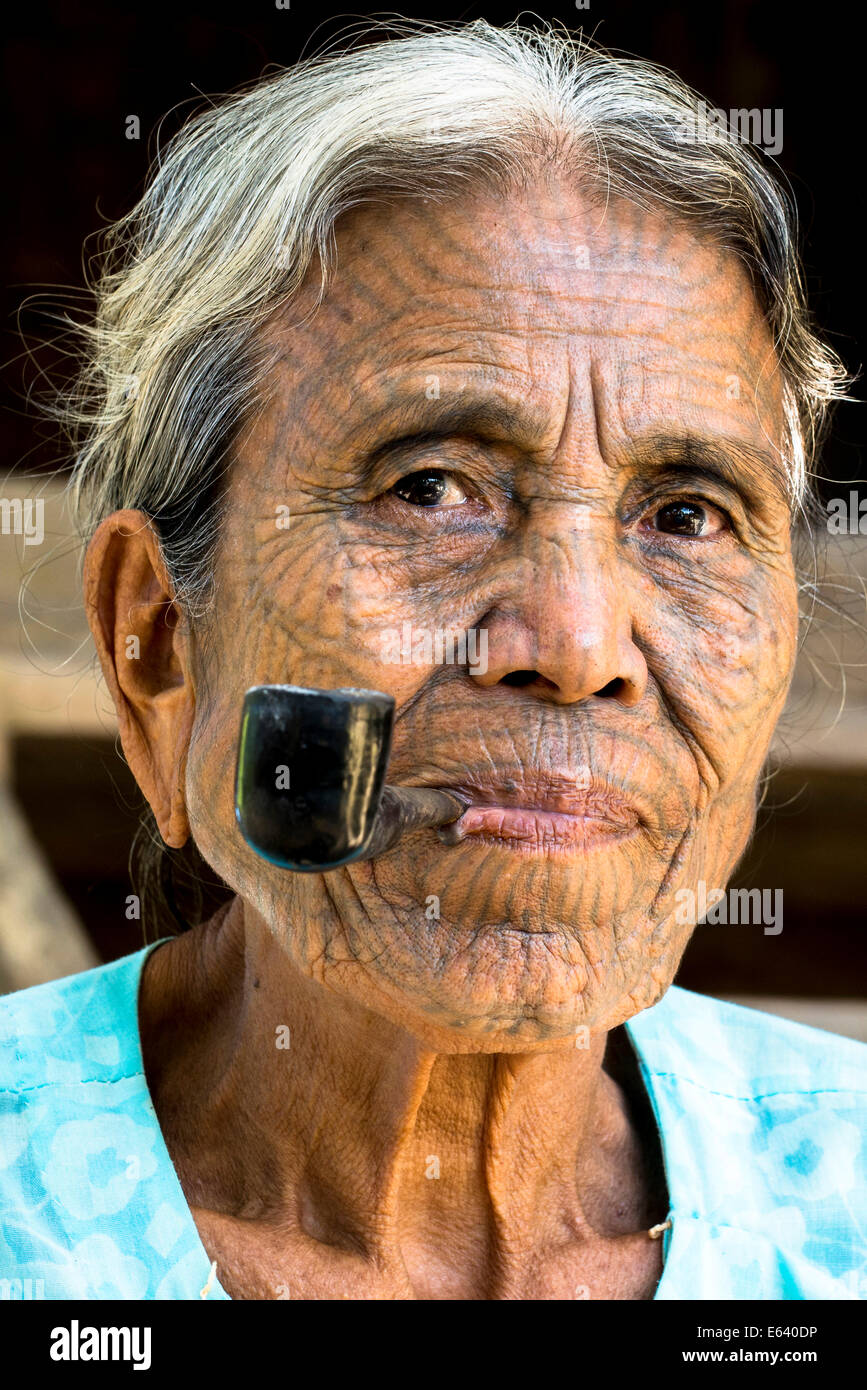 Frau aus dem Volk der Chin, ethnische Minderheit mit einer traditionellen Gesichts-Tätowierung raucht eine Pfeife, die letzten ihrer Art Porträt Stockfoto