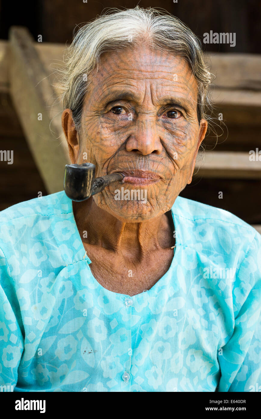 Frau aus dem Volk der Chin, ethnische Minderheit mit einer traditionellen Gesichts-Tätowierung raucht eine Pfeife, die letzten ihrer Art Porträt Stockfoto