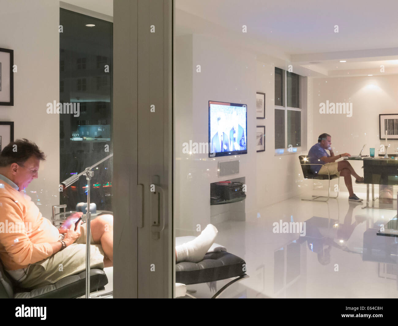 Reife Männer lesen in Luxus-Showcase-Eigentumswohnung, Blick vom Balkon in der Abenddämmerung, Fort Lauderdale, FL, USA Stockfoto