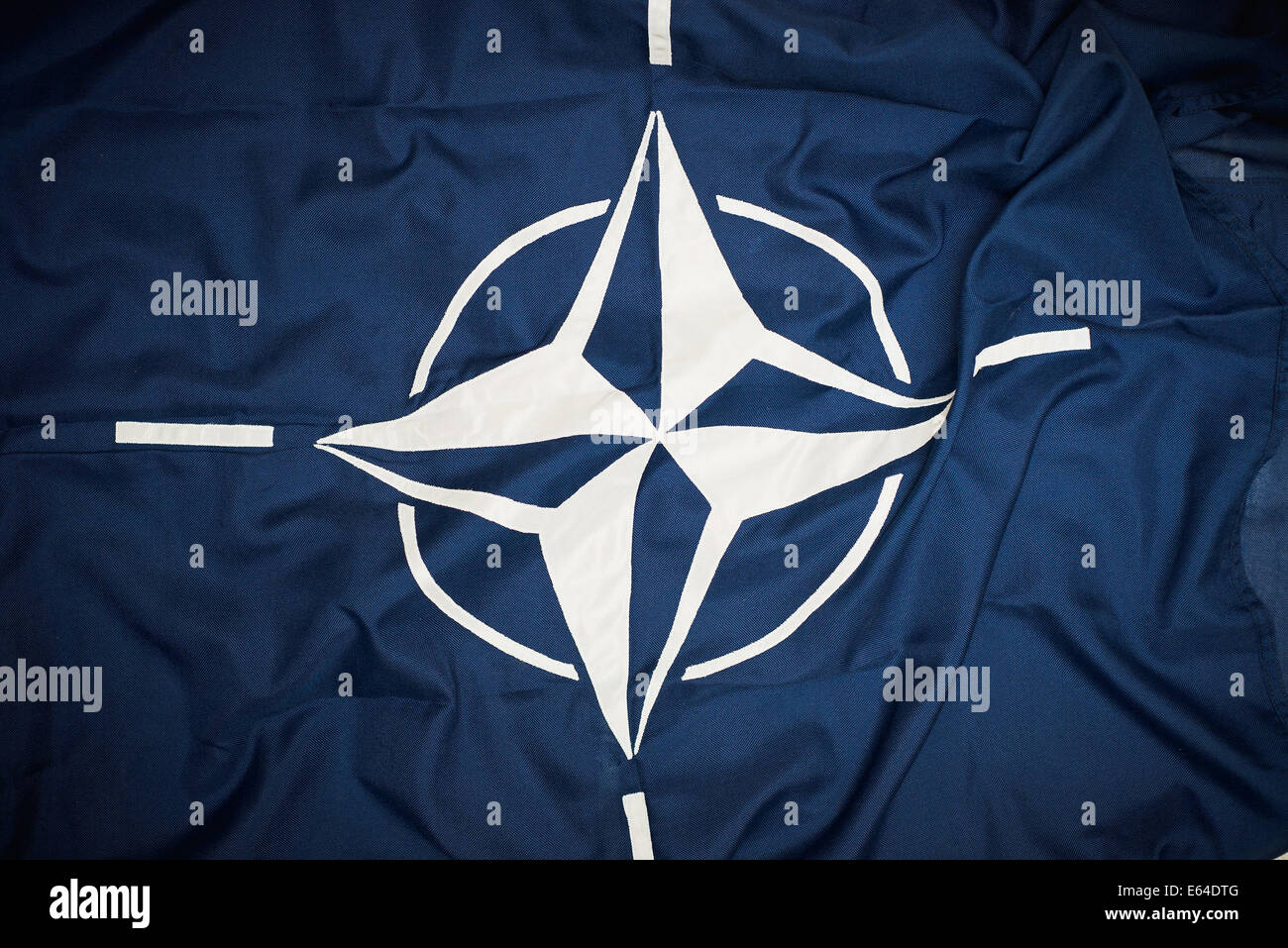 Die Flagge der NATO zeigt ein dunkelblaues Feld mit einem weißen Kompassrosenemblem, das den Zweck der Organisation symbolisiert, Frieden und Stabilität zu fördern. Die vier weißen Linien erstrecken sich von den Kardinalpunkten und spiegeln die globale Reichweite der NATO wider. Stockfoto