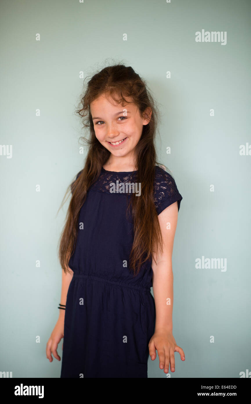 Glücklich lächelnd braunen Haaren 10 jährige Pre Mädchens steht man vor einer grünen Wand UK Stockfoto