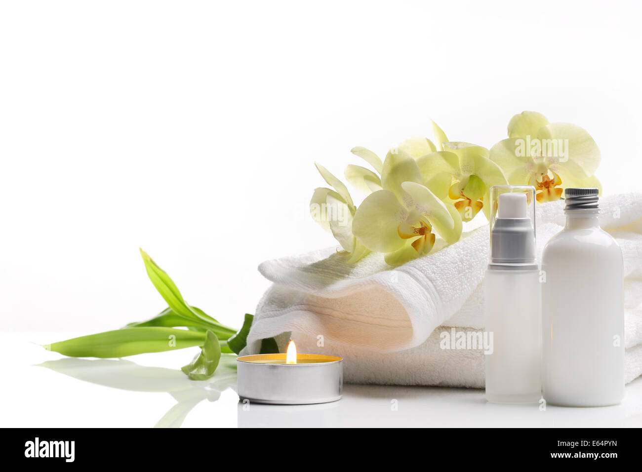 Spa-Stillleben mit Handtuch, brennende Kerzen und Blumen auf weißem Hintergrund. Stockfoto