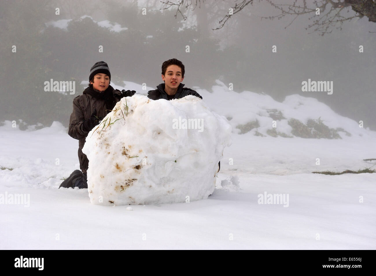 Kinder spielen - jungen im Teenageralter Rollen einen riesigen Schneeball bergab im Schnee im Winter Stockfoto