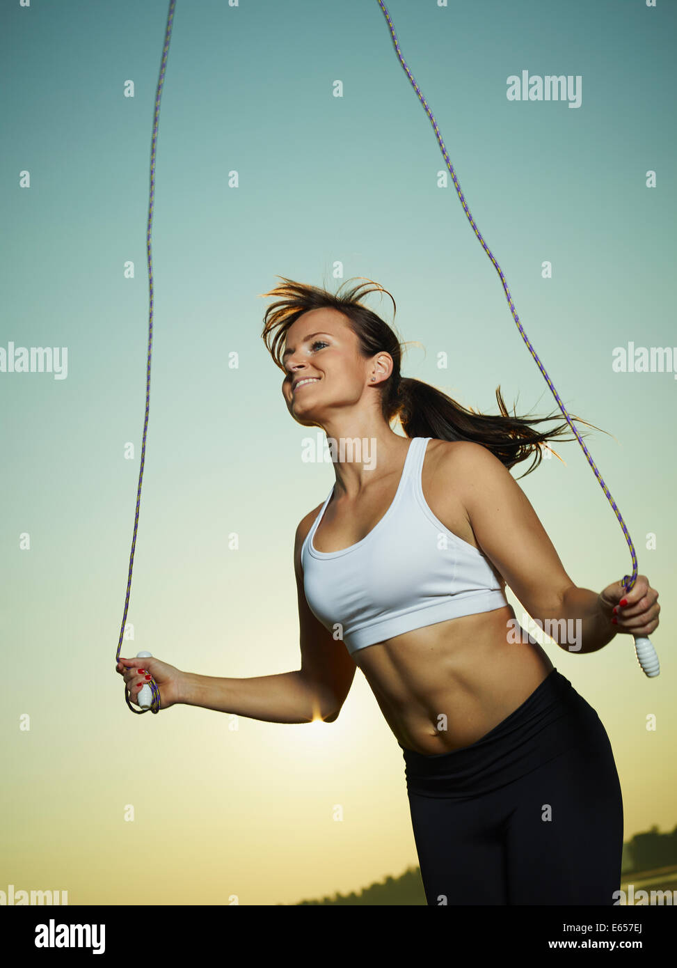 Junge Fitness Frau benutzt ein springen Seil, Sonne und Himmel auf Hintergrund Stockfoto