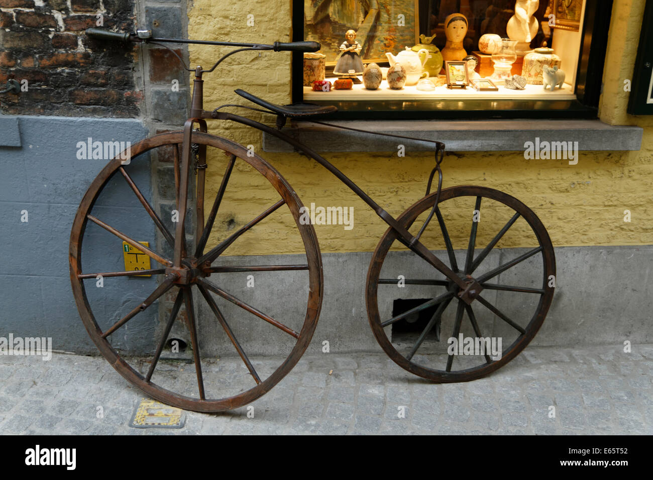 19. century​ Fahrrad lehnt sich gegen ein antiquitätenladen an der Wand und die beleuchteten Fenster in Brügge: Stockfoto