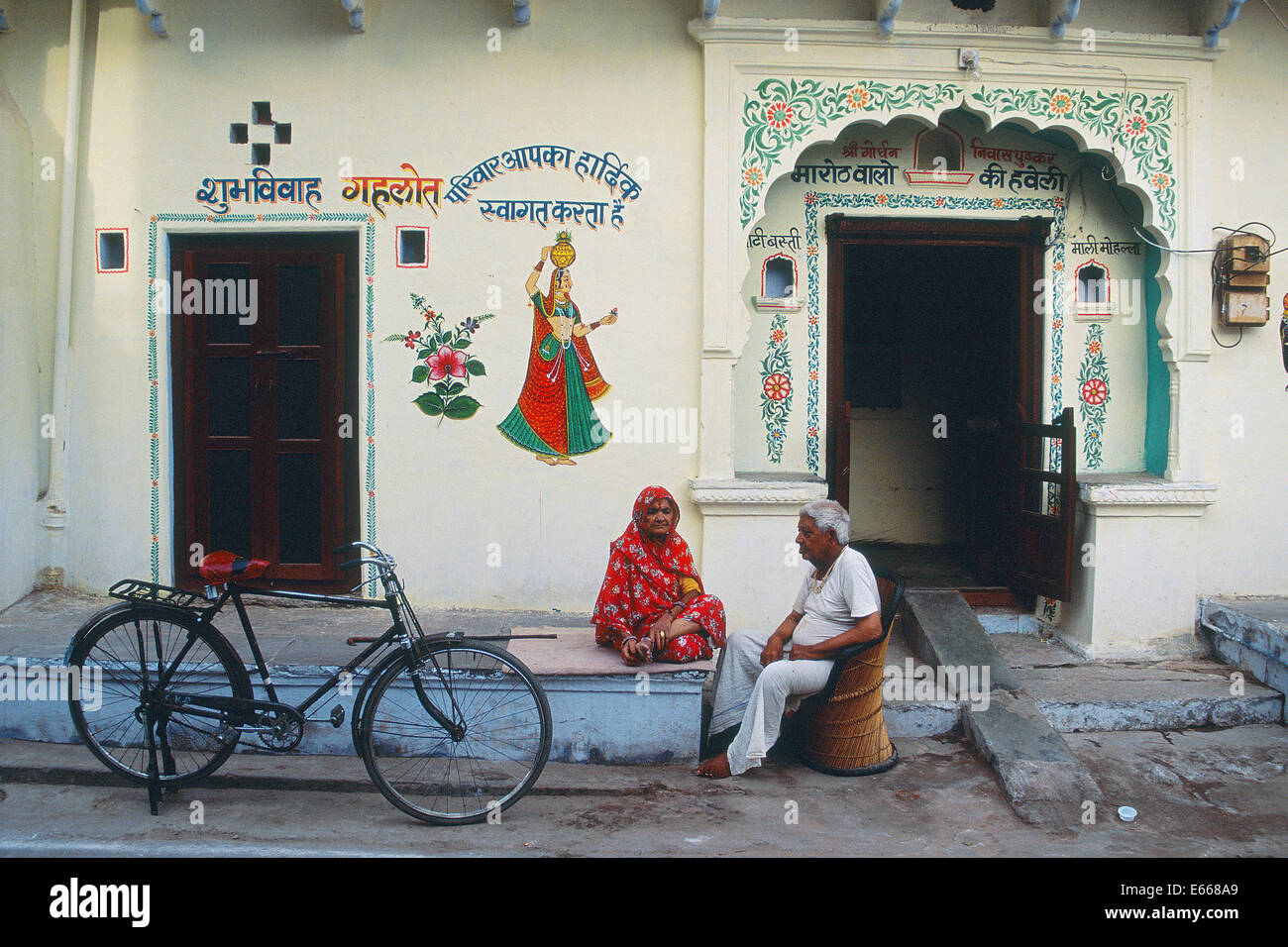 Ein Alter Mann und alte Frau sprechen auf der Straße vor einem traditionell bemalten Haus (Indien) Stockfoto