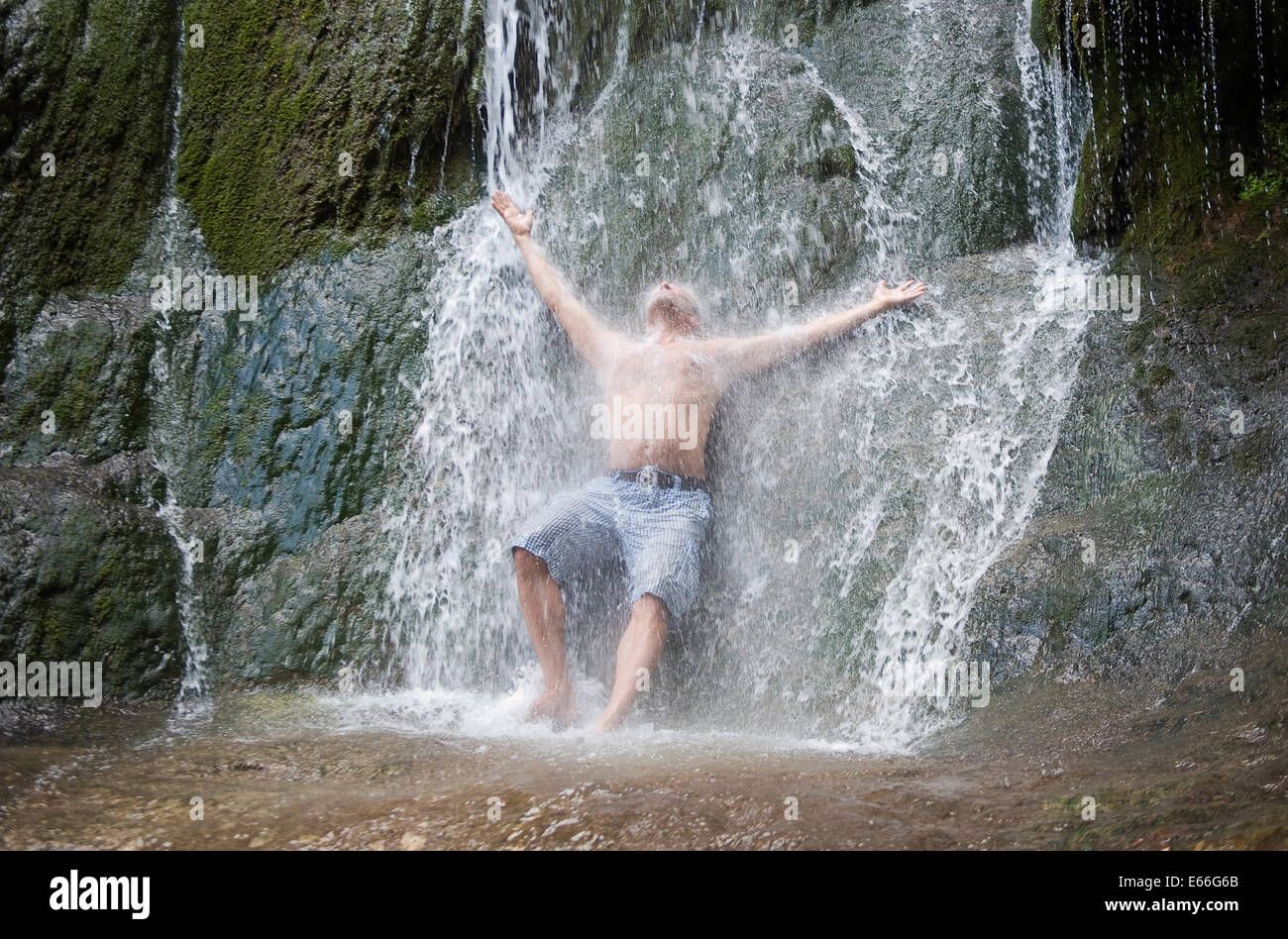 Ein Mann hat eine Dusche unter einem natürlichen Wasserfall Stockfotografie  - Alamy