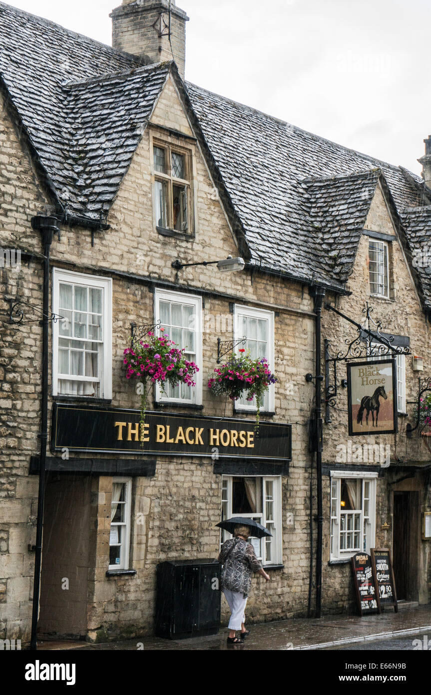 Frau vorbei gehen. Das schwarze Pferd Public House im Regen, Stadtzentrum, Cirencester, Cotswolds, Gloucestershire, England, UK. Stockfoto