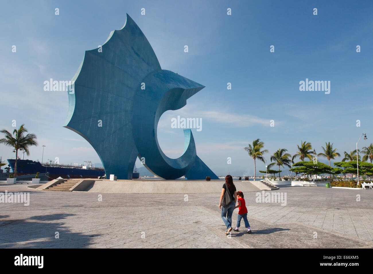 Mutter und Tochter gehen in der Plaza in der Nähe einer riesigen Sailfish-Statue in Manzanillo, Colima, Mexiko Stockfoto