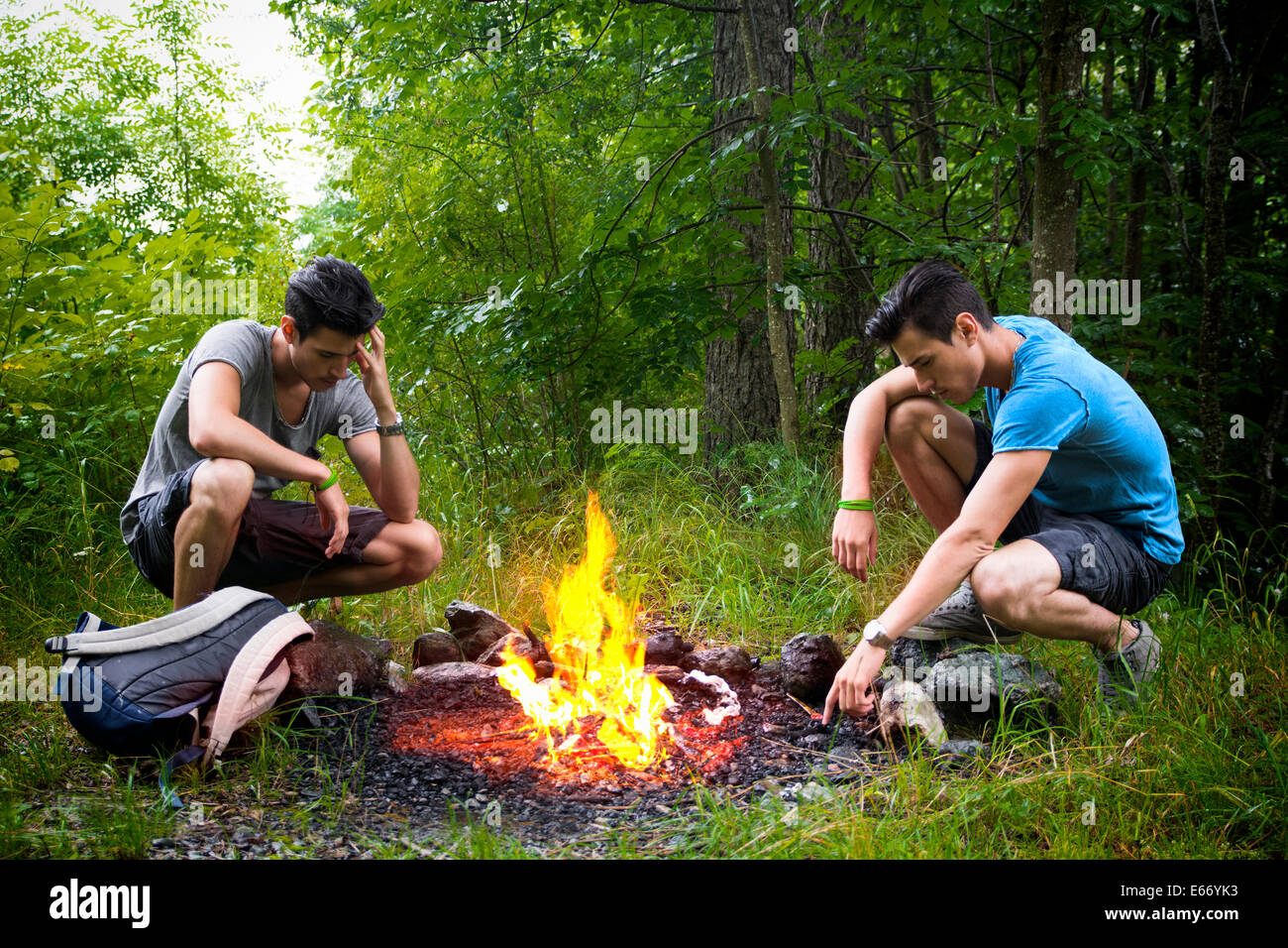 Zwei junge Männer, die camping in den Bergen hocken neben einem brennenden Lagerfeuer mit Rucksack starrte nachdenklich auf das Feuer Stockfoto