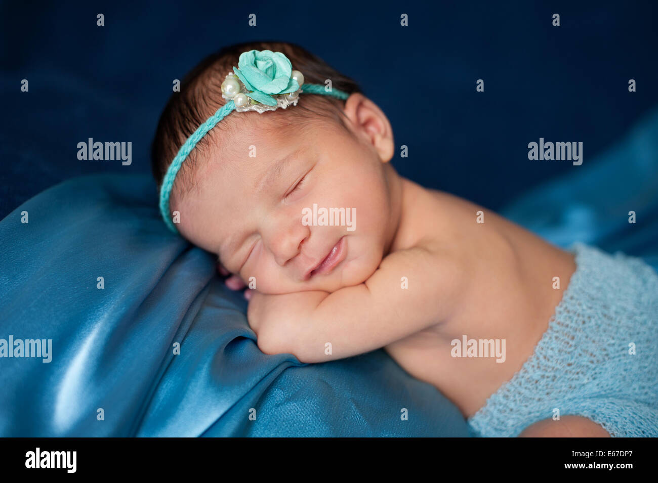 Sechs Tage altes neugeborenes Mädchen tragen eine Papier rose und Perle Stirnband und schlafen auf blauem Stoff. Stockfoto