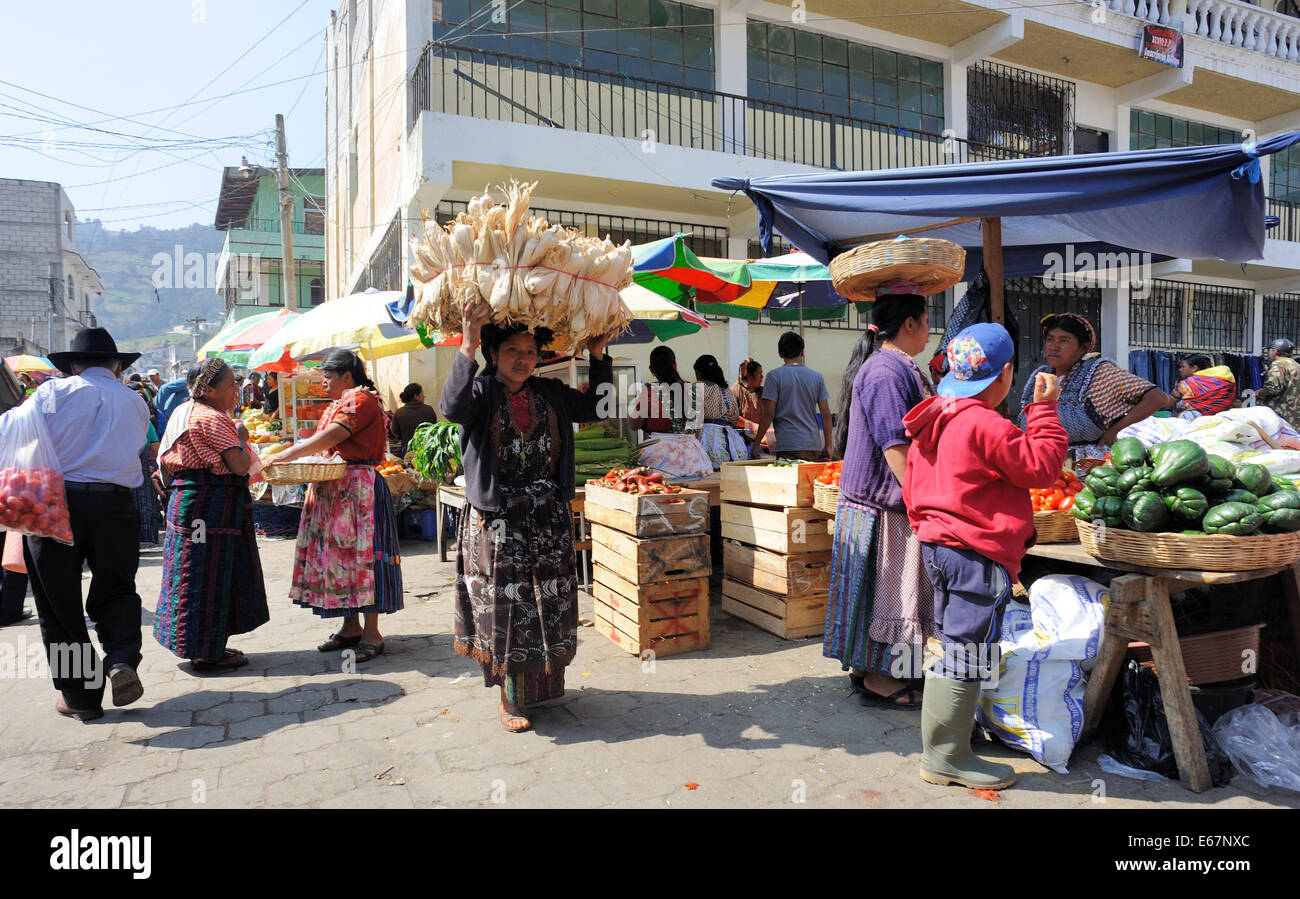 Eine Frau trägt eine Last von Mais oder Maiskolben auf dem Kopf, die letzten Leute verkaufen Obst und Gemüse auf dem Markt am Almolonga. Stockfoto