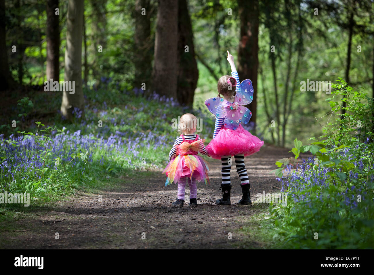Zwei Mädchen im Märchen Kleider zu Fuß durch eine englische Bluebell Holz im Frühjahr. Stockfoto