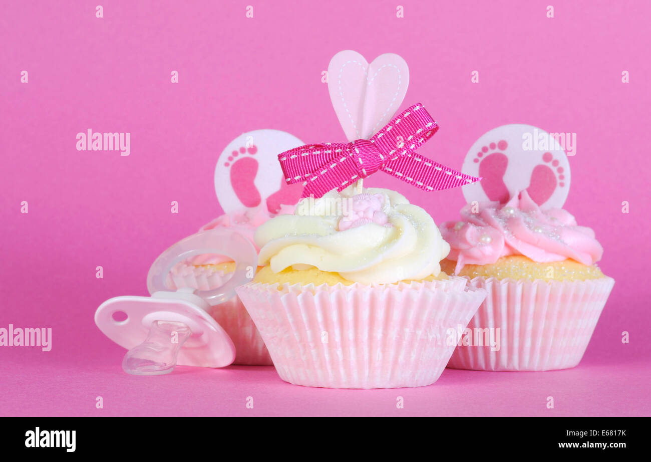 Rosa Thema Baby Mädchen drei Cupcakes mit Dummy-Schnuller vor einem rosa Hintergrund Stockfoto