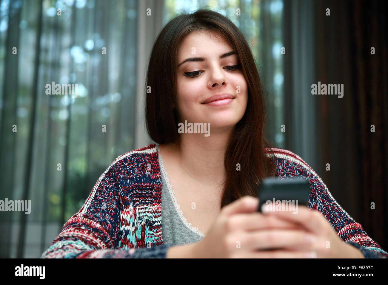 Attraktive Frau mit Smartphone zu Hause lächelnd Stockfoto