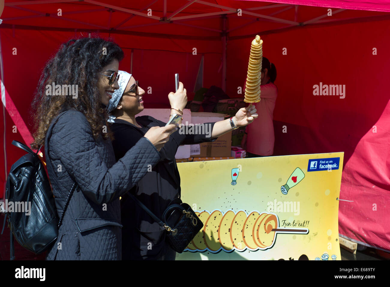 Battersea Park, Food Festival. London UK. 17. August 2014 zwei Frauen fotografieren ihre Kartoffel-Strudel auf ihre Smartphones. Stockfoto