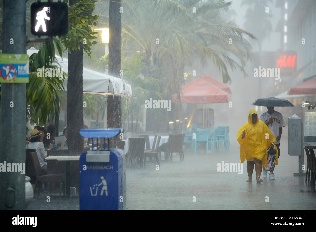 Ein Mann hält einen Regenschirm und eine Frau trägt einen Regenmantel, sich fernzuhalten Stockfoto
