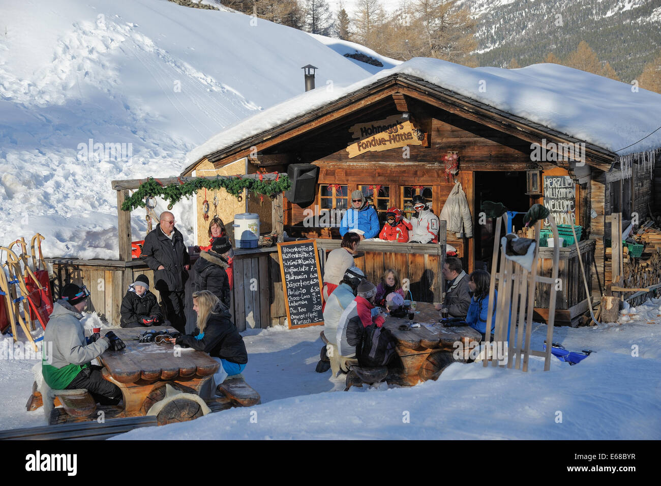 Kleines Restaurant mit Schweizer Fondue. Kunden haben Getränke im Freien im Schnee unter Ausnutzung der letzten Sonnenstrahlen Stockfoto