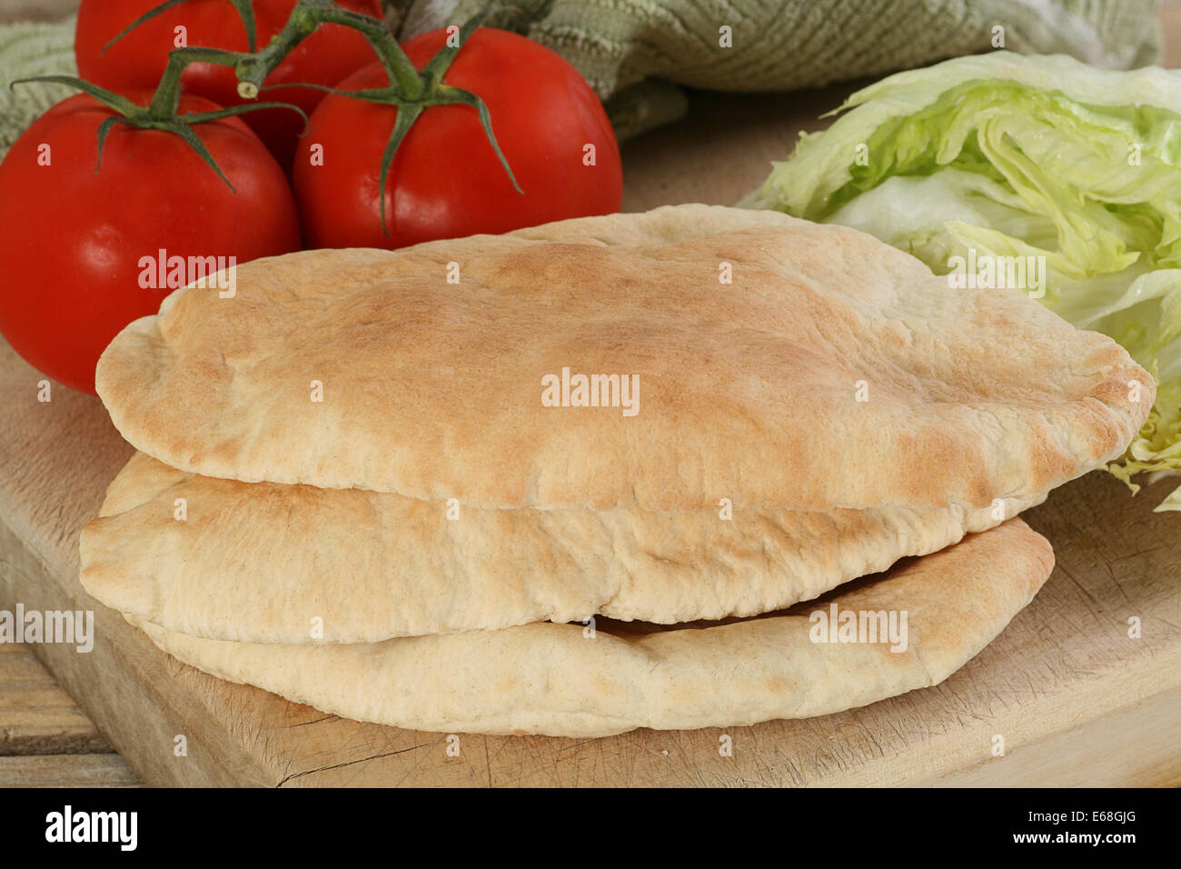 Stapel von drei frische Pitta-Brot auf einem Holzbrett mit Salat und Tomate Stockfoto