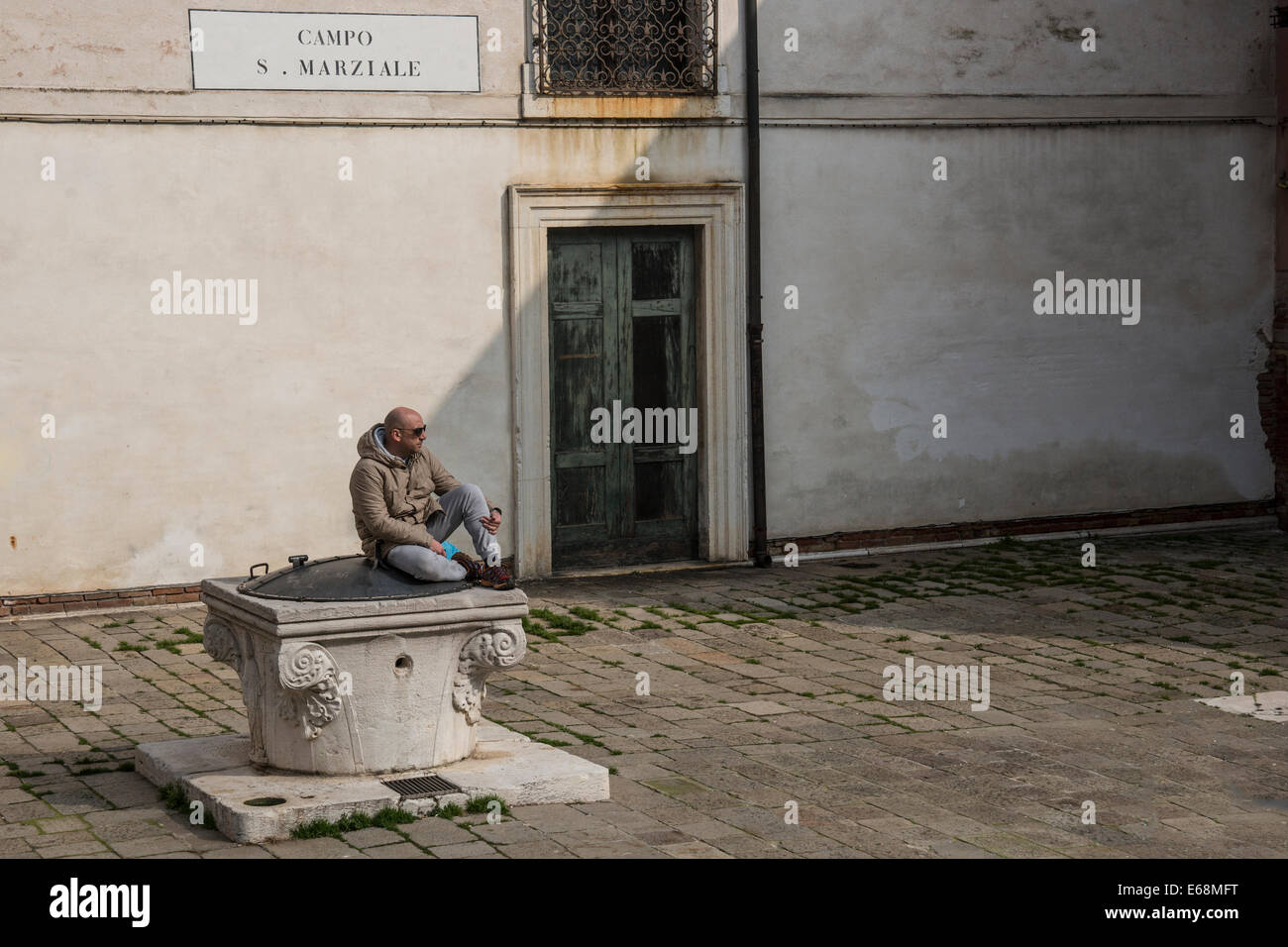 Mann sitzt Don die überdachte gut und blickt auf die verlassene Campo San Marziale in Venedig. Stockfoto