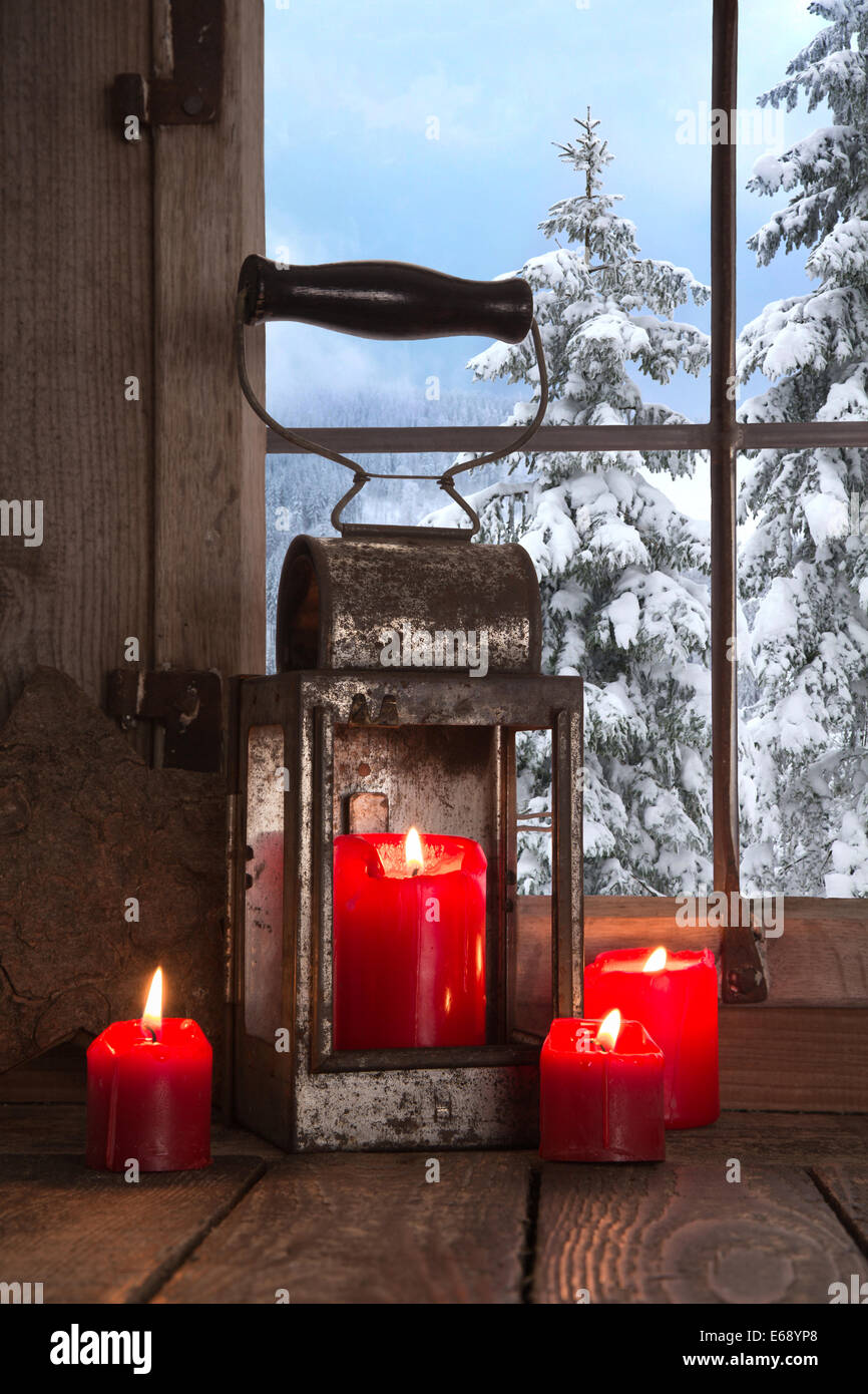 Alte hölzerne Fensterbank dekoriert mit vier roten Weihnachtskerzen. Blick auf den verschneiten Bäumen in den Bergen. Stockfoto