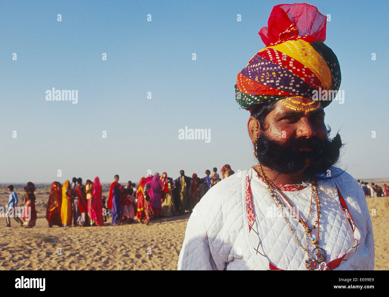 Traditionell gekleidete hindu Mann. Er gehört zu der Rajput-Klasse. Im Hintergrund sind einheimische Frauen sichtbar (Indien) Stockfoto