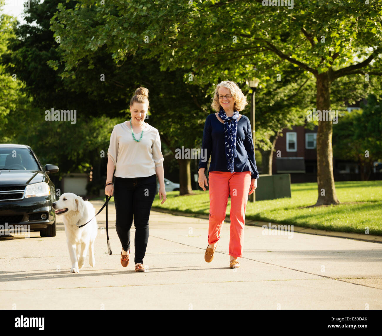 Kaukasische Mutter und Tochter Spaziergang mit Hund auf Vorort Straße Stockfoto
