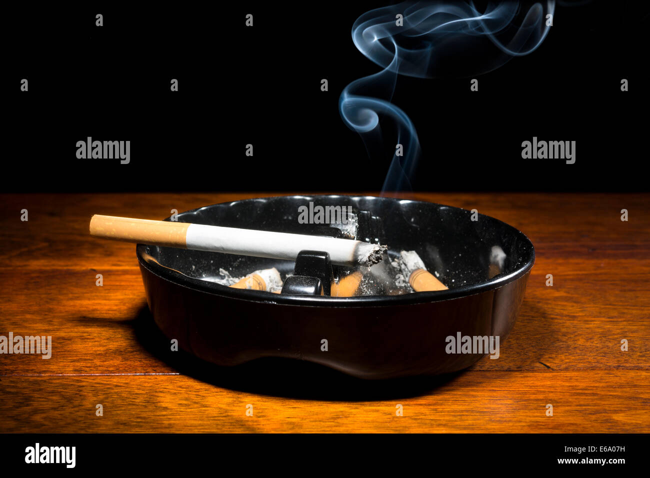 Eine brennende Zigarre in einem klassischen schwarzen Aschenbecher Streaming-Rauchen in einem dunklen, stimmungsvolle Ambiente. Stockfoto