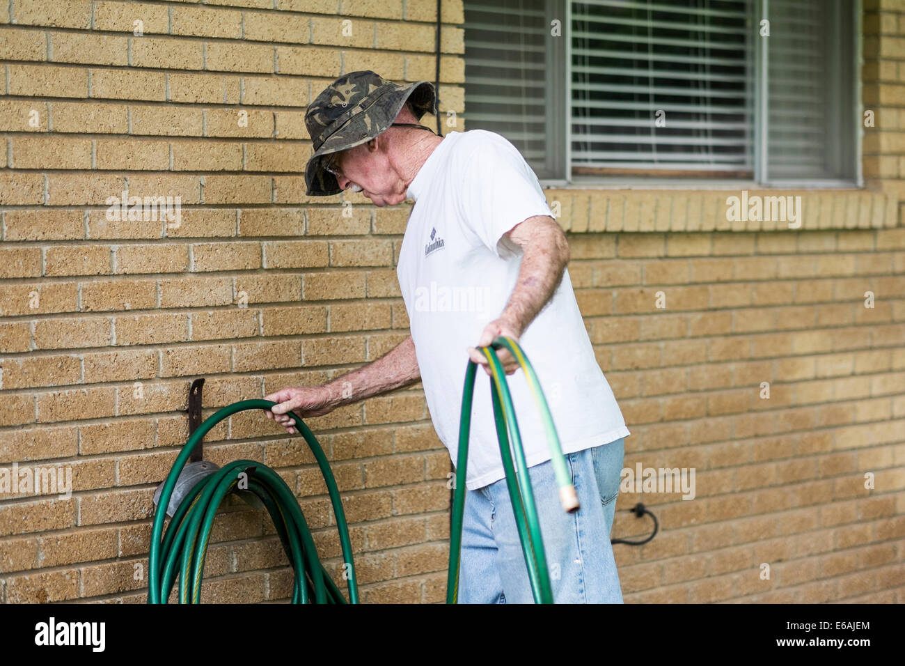 Ein 76 Jahre alter Kaukasischer mann Spulen mit einem Wasserschlauch gegen das Haus im Freien. USA. Stockfoto