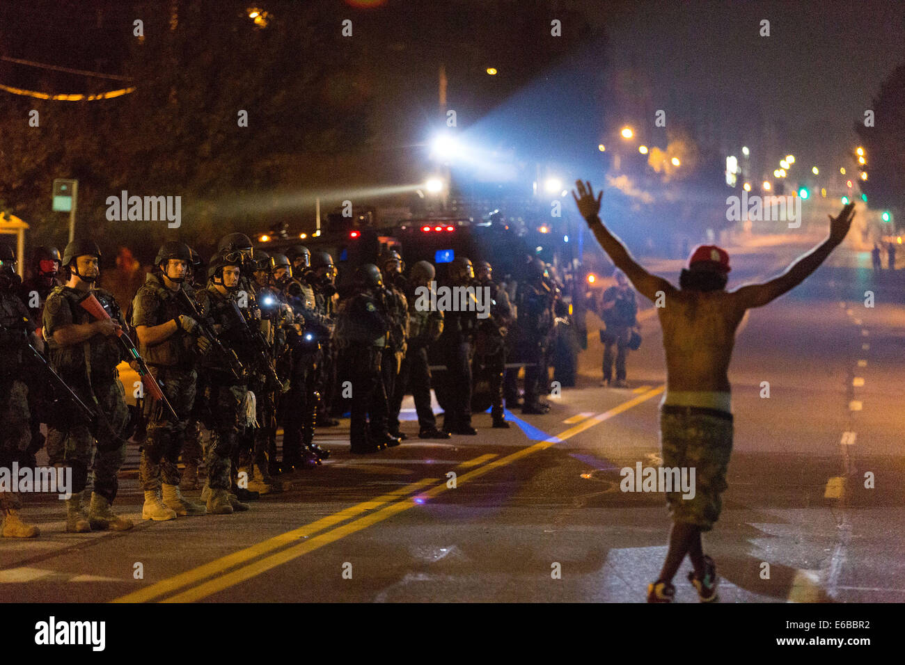 Ferguson, USA. 18. August 2014. Ein Demonstrant hält seine Hände hoch Gesänge "Hände hoch, Don't shoot" als SWAT Polizeieinheit steht Wache während der Proteste gegen das Töten der Polizei von Michael Brown, Ferguson, Missouri, Vereinigte Staaten, etwa um Mitternacht des 18. August 2014. Am 9. August wurde 18-j hrige Afroamerikaner Michael Brown von Polizei in Ferguson, Funkenbildung kontinuierlichen Proteste in der Stadt, wo der Großteil der Bevölkerung ist schwarz, erschossen. Bildnachweis: Shen Ting/Xinhua/Alamy Live-Nachrichten Stockfoto