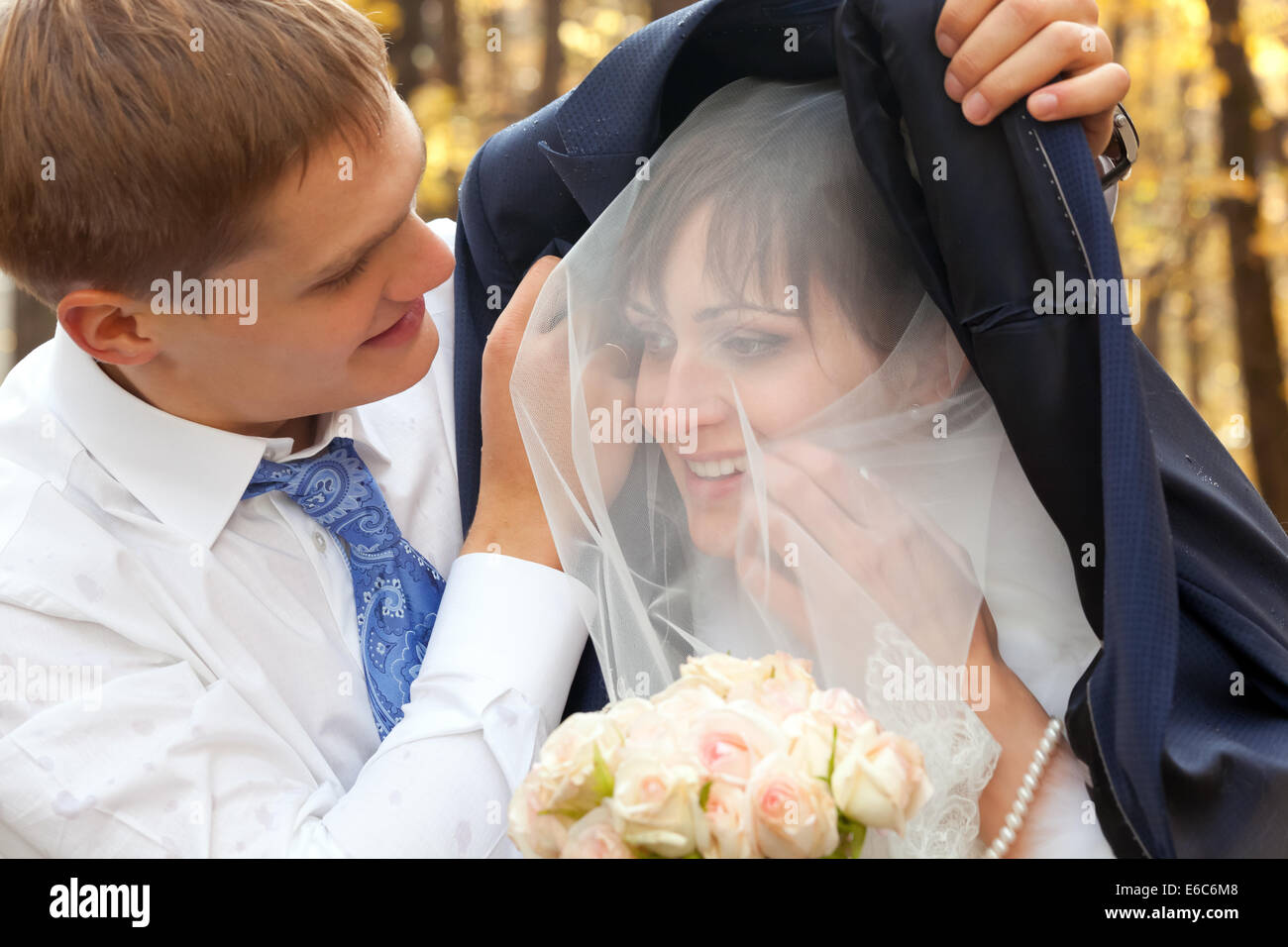 Bräutigam seine schöne Braut vor Regen zu schützen Stockfoto