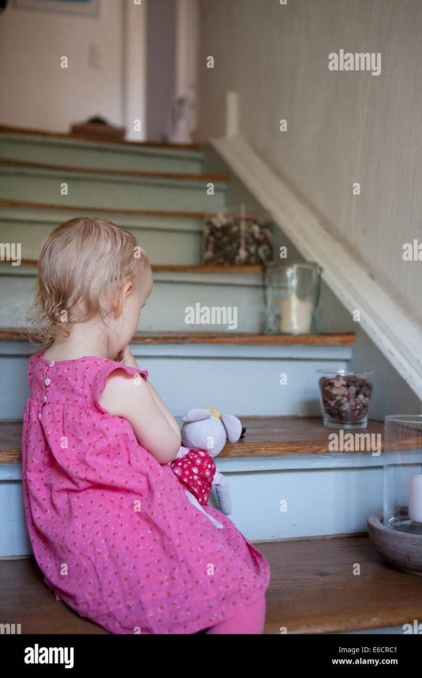 Mädchen im rosa Kleid, sitzt auf der Treppe in einem Haus mit ihr Stofftier. Stockfoto