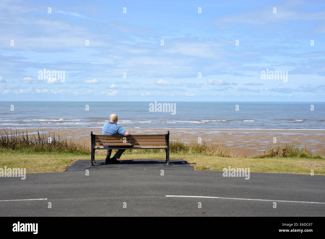 Einsame ältere Mann sitzt auf Holzbank mit Blick aufs Meer in Blackpool, Lancashire. Stockfoto