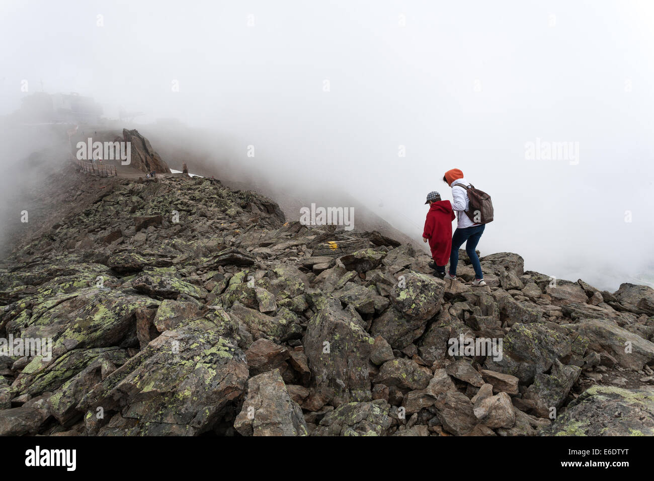 eine Frau mit Rucksack und ihrem jungen in rotes langes Sweatshirt im Nebel zu Fuß auf einem großen Felsen in Alpen Stockfoto