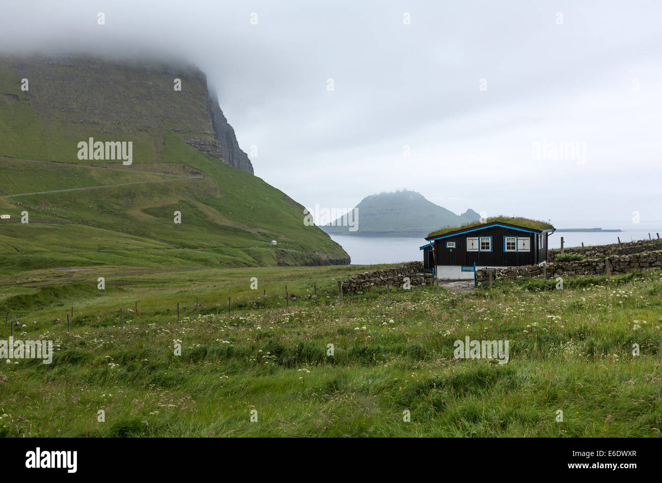 Gasadalur Dorf mit einem Rasen Rasen bedeckt Haus und der Tindhólmur-Insel. Vagar, Färöer Insel Stockfoto