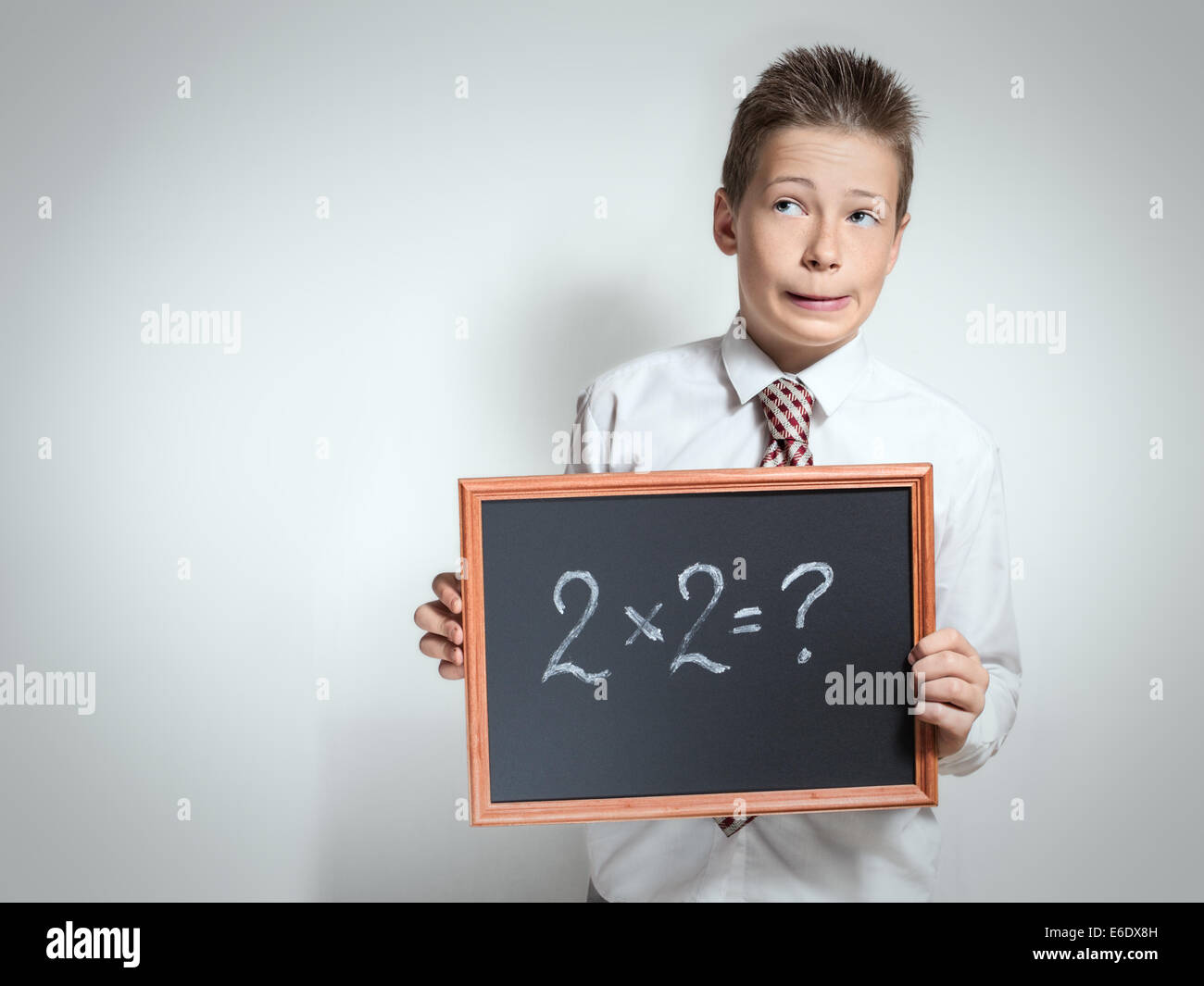 Der nette lustige Schuljunge Teenager in ein weißes Hemd denken über die Entscheidung der Aufgabe auf die schwarze Tafel Stockfoto