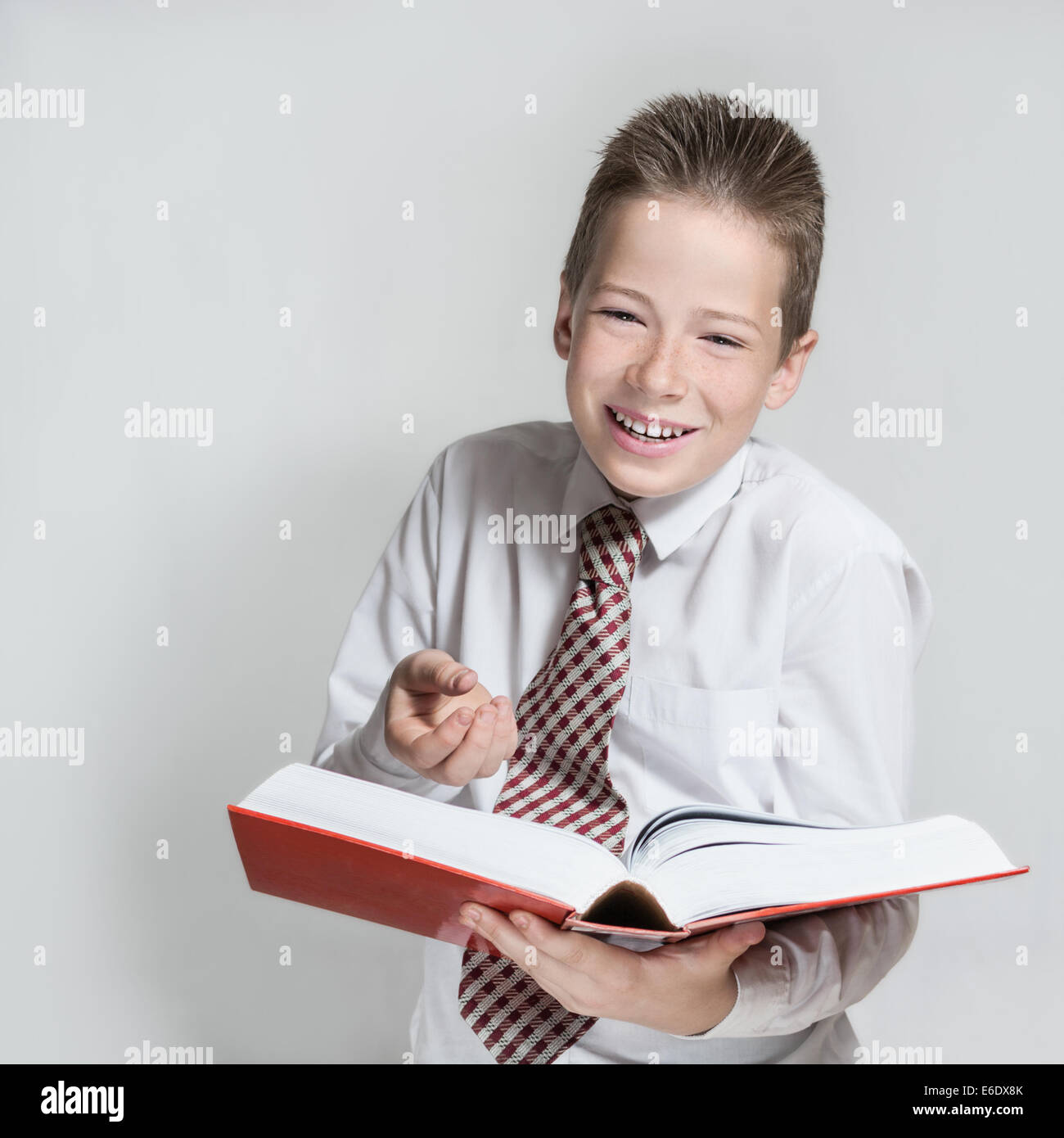 Die lächelnde junge Teenager in ein weißes Hemd und eine Krawatte liest ein große rote lustiges Buch Stockfoto