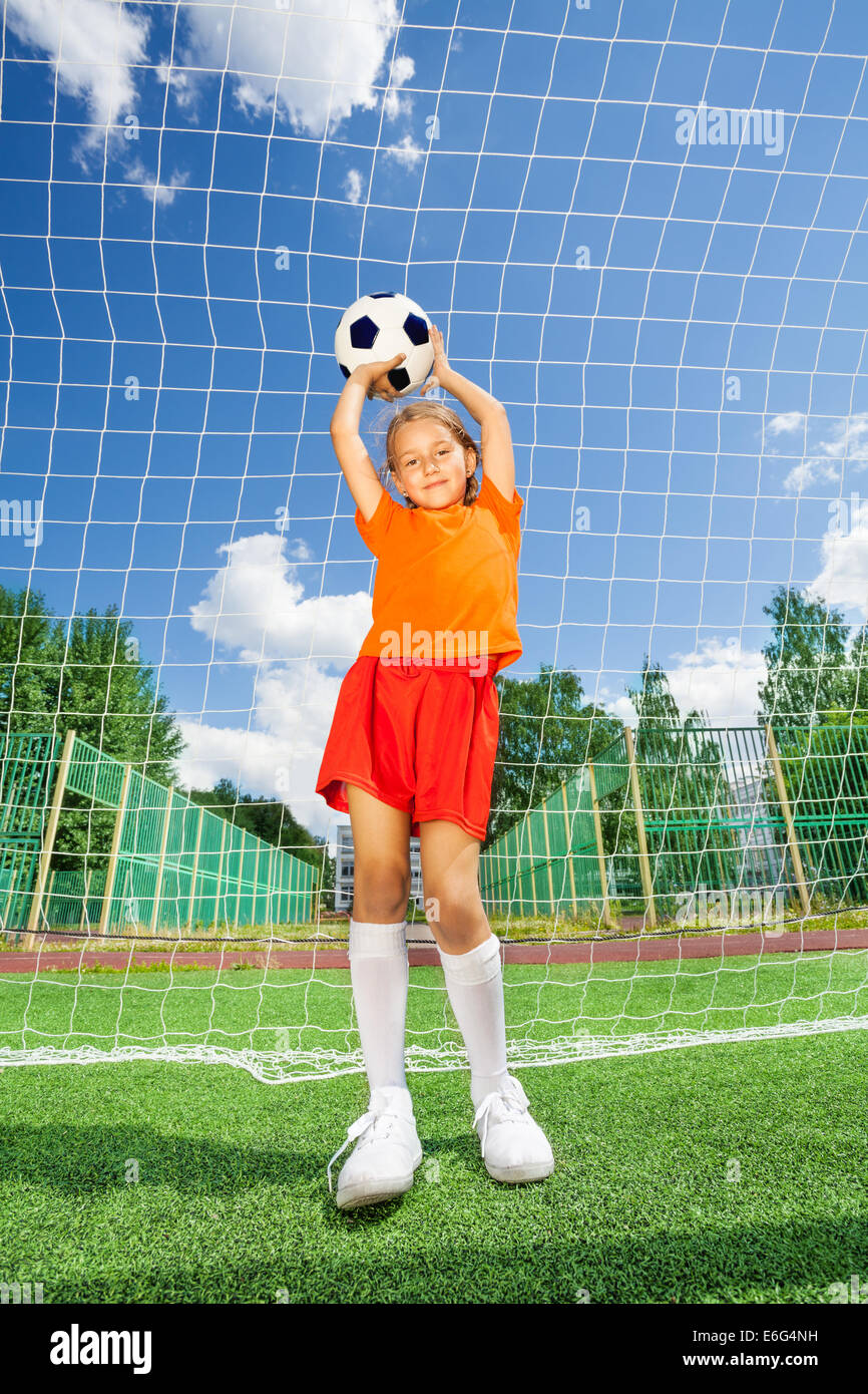 Mädchen Fußball auf beiden gestreckten Armen halten Stockfoto