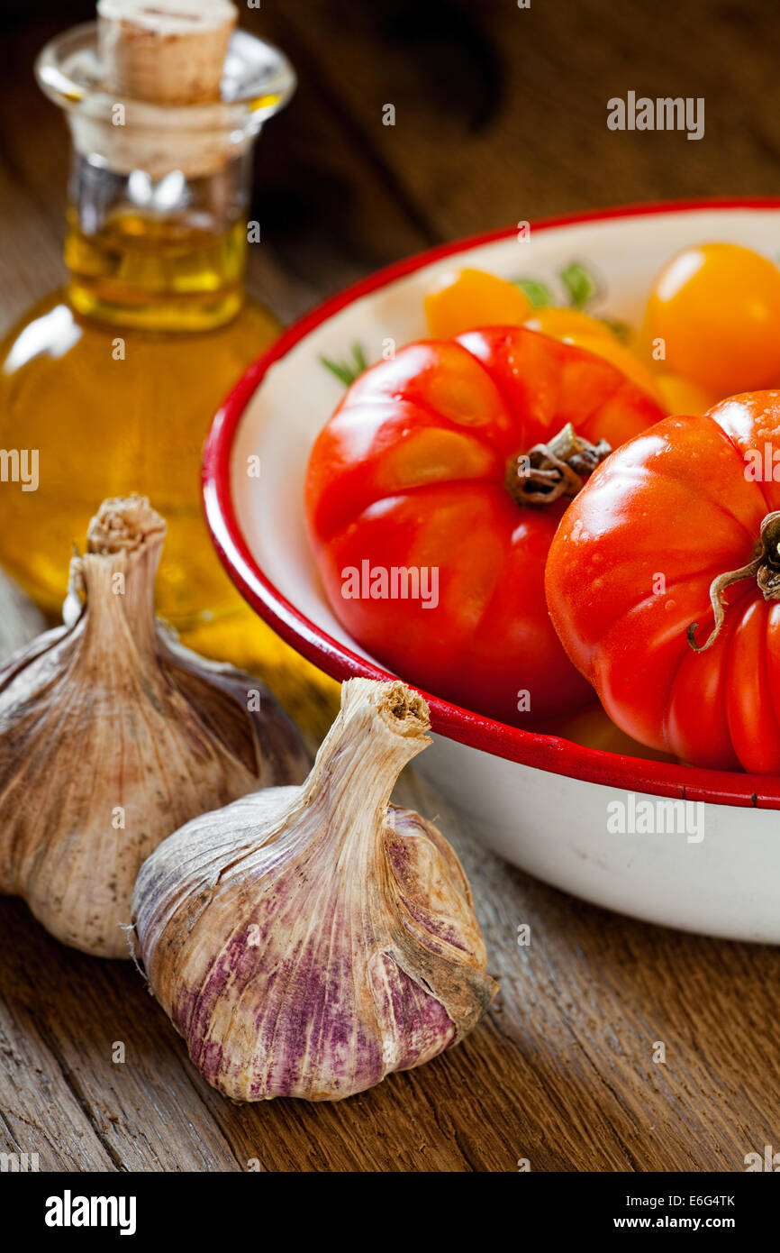 Frisch gepflückten Tomaten in einem Emaille Schüssel Fleisch, Knoblauch Zwiebeln und eine Flasche Olivenöl Stockfoto