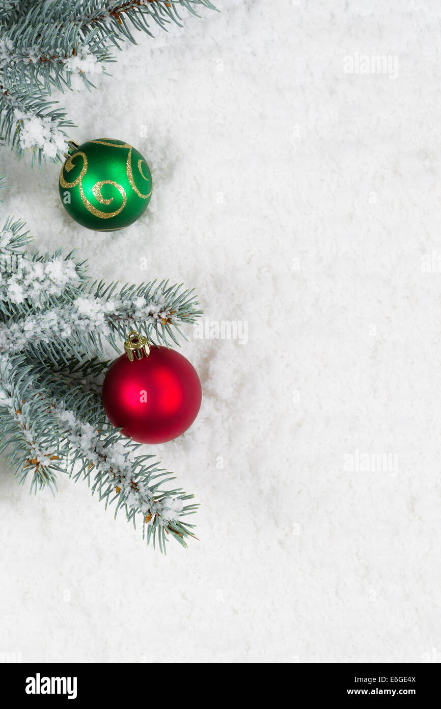 Vertikales Bild von Weihnachtsschmuck, rot und grün, hängend von einem echten Blaufichten Ast gelegt auf Schnee Stockfoto