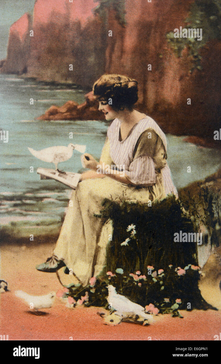 Bezaubernde Lage am Meer mit einer Frau, die Vögel auf einer alten Postkarte aus dem frühen 20. Jahrhundert liest und füttert Stockfoto