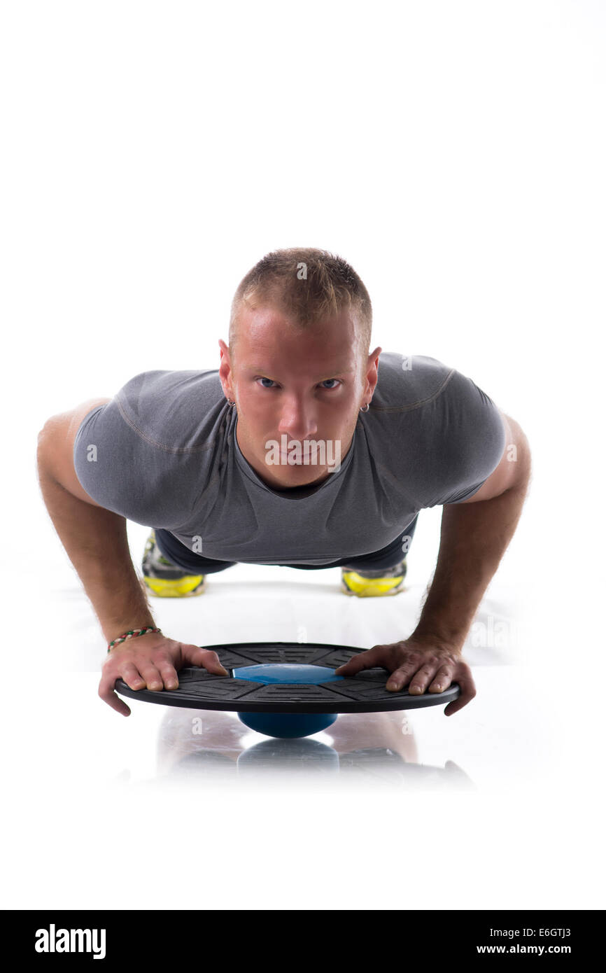 Junge blonde muskulöser Mann Ausübung auf dem Boden mit Balance Disc Board isoliert auf weiss Stockfoto