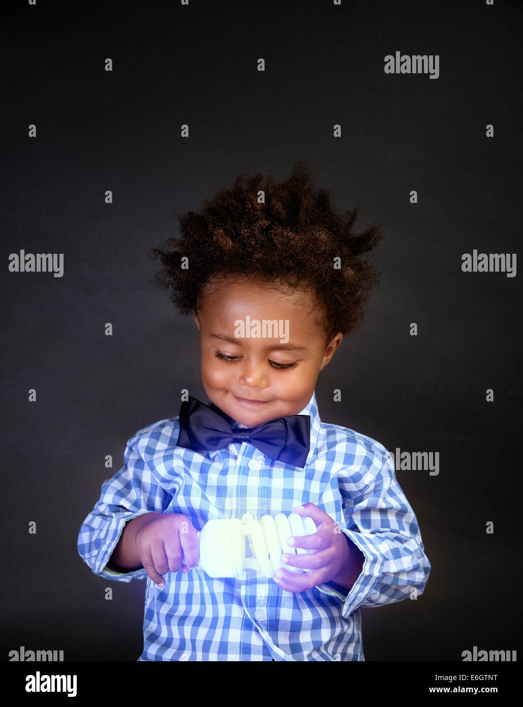 Porträt von niedlichen kleinen afrikanischen Schuljunge hält in Händen helle Lampe, isoliert auf schwarzem Hintergrund, Innovation und Erfindung Stockfoto